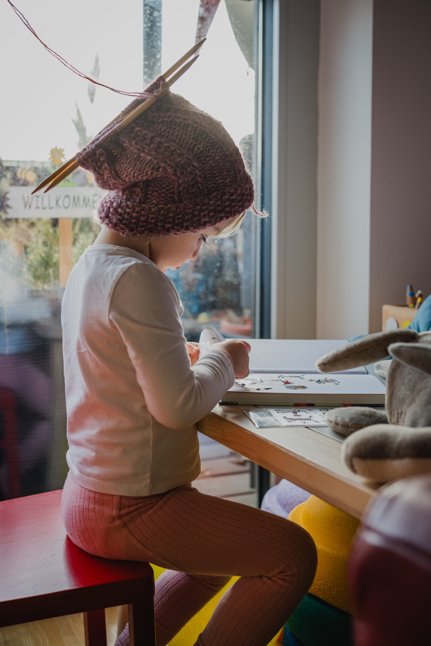 Mädchen mit Haube sitzt am Tisch, in dem noch Häkelnadeln stecken – dokumentarische Familienfotografie in Graz