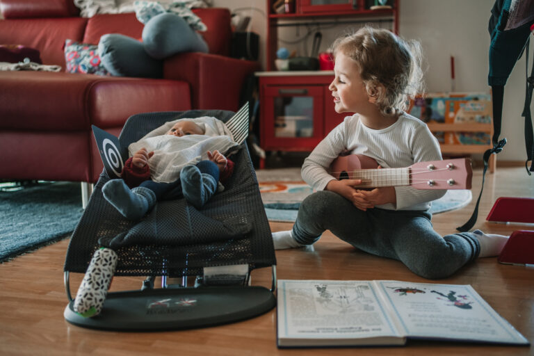 Kleinkind spielt Gitarre für Baby in der Wippe. echte Familienfotos