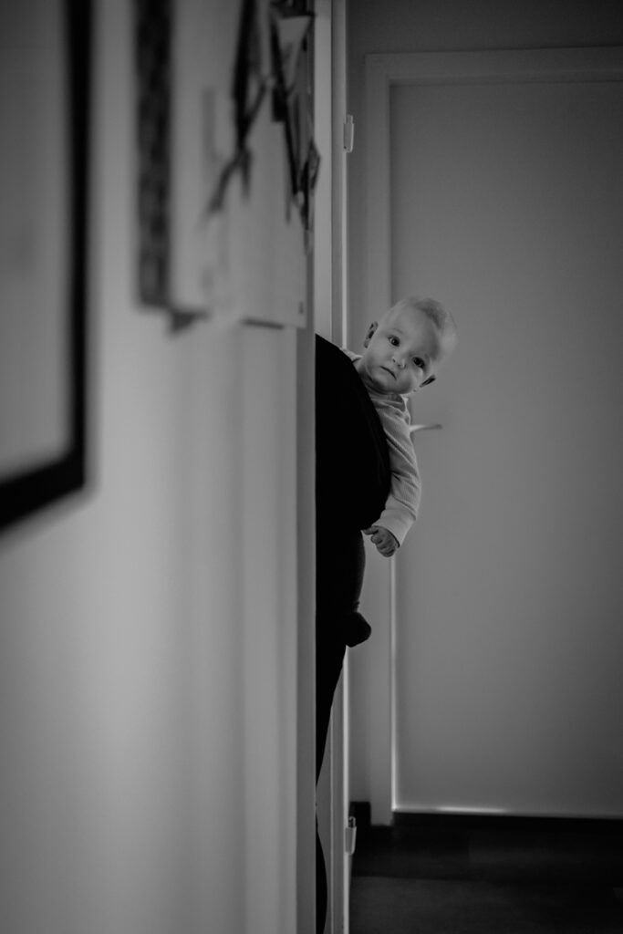 Baby schaut neugierig auf Mamas Arm ums Eck – natürliche Familienfotografie Graz und Umgebung