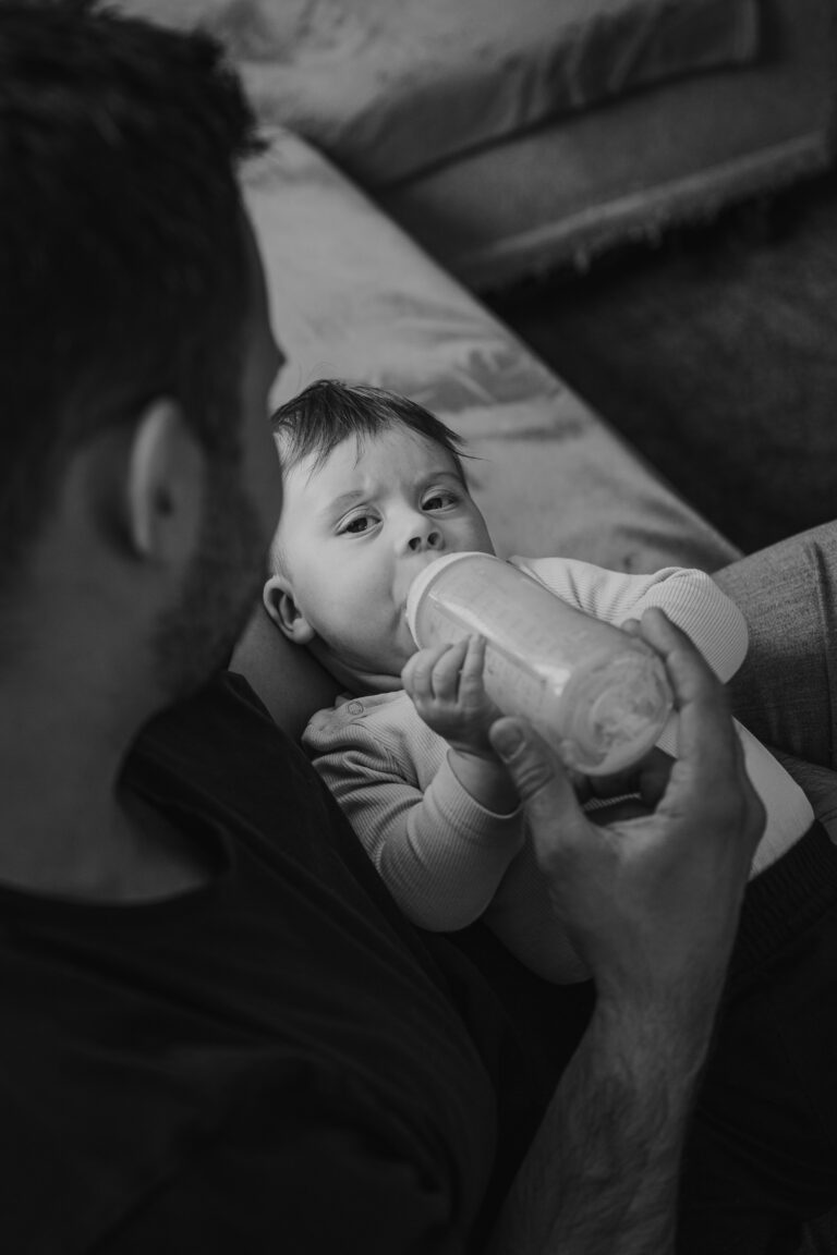 Baby trinkt aus der Flasche und schaut intensiv zu Papa – authentische Familienfotos Graz und Umgebung