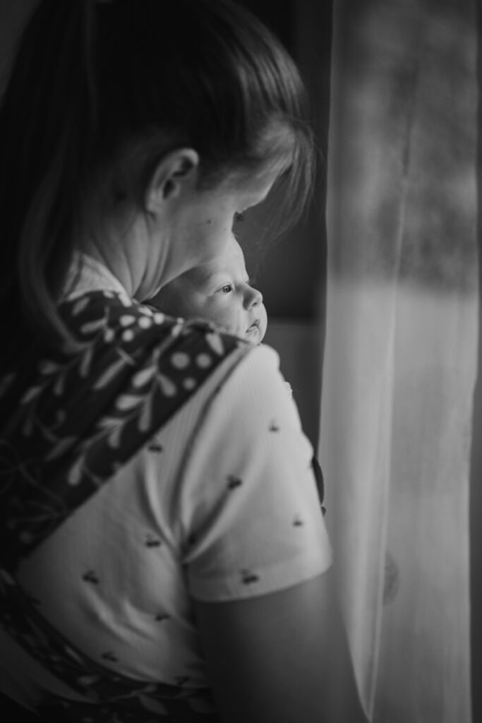 Baby in der Trage schaut neugierig aus dem Fenster – dokumentarische Familienfotografie in Graz und Graz Umgebung