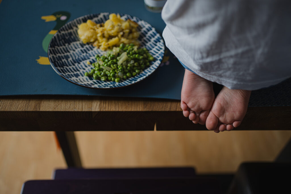 zu sehen sind Kinderfüße am Tisch neben einem vollen Teller. echte Familienfotografie graz