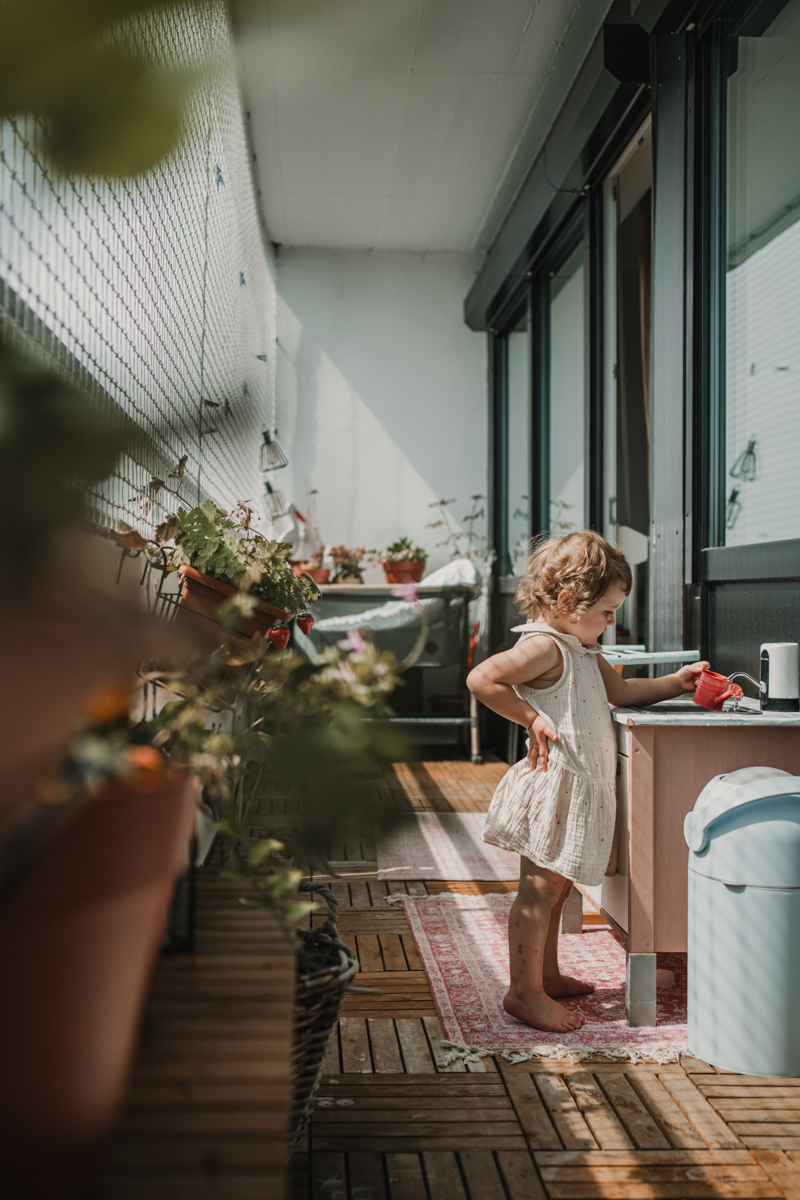 kleines Mädchen am Balkon. füllt Gießkanne mit Hand auf der Hüfte. Familienfotografie graz
