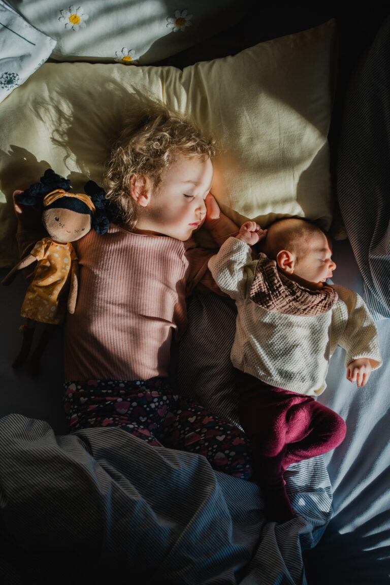 zwei Geschwister liegen schlafend im Bett, die sonne wirft schönes licht, newborn authentisch graz