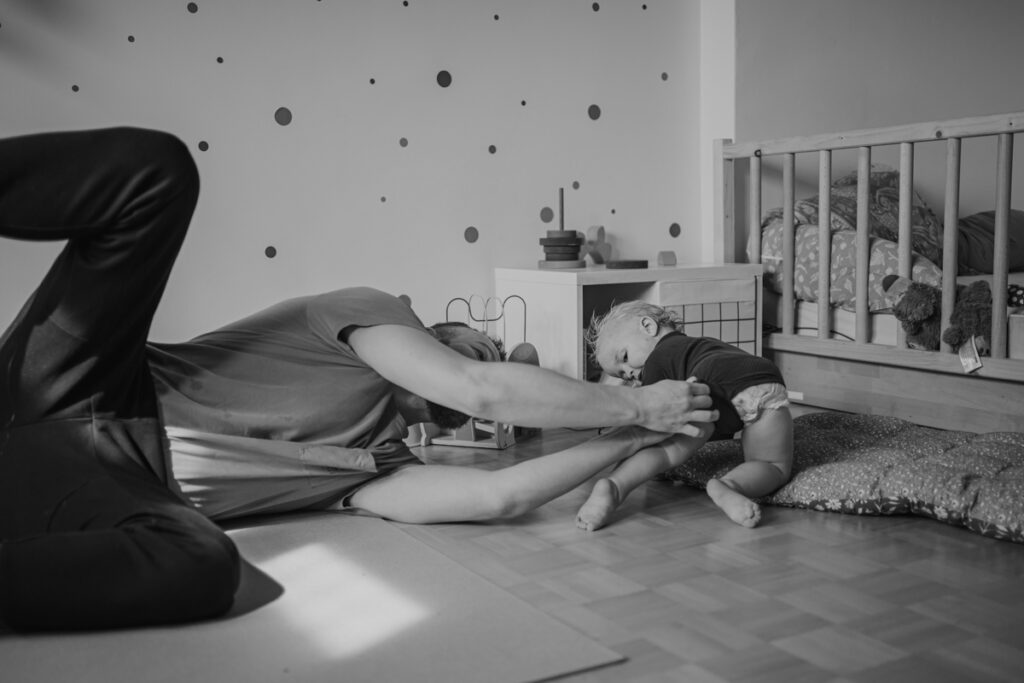 Papa macht Kleinkind den Body zu, während es wegkrabbelt – dokumentarische Familienfotografie Graz und Umgebung, authentische Alltagsszenen