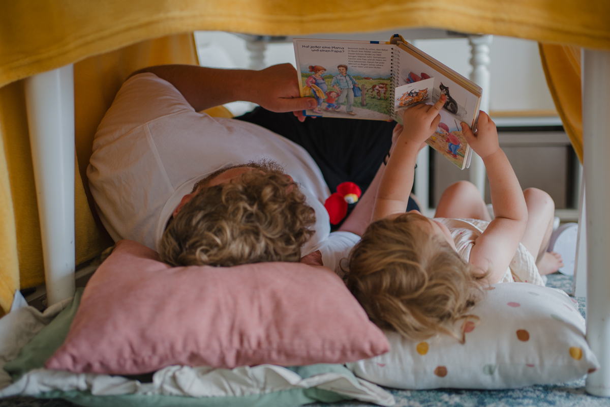Papa und Tochter lesen gemeinsam unter dem Tisch – authentischer Familienalltag in Graz und Umgebung