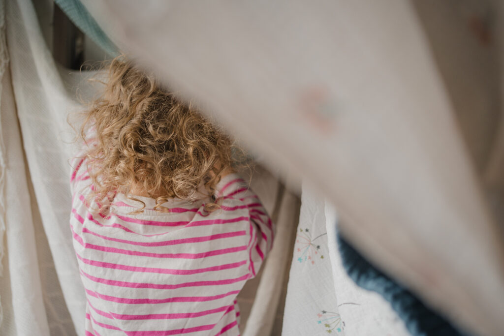 Lockenköpfiges Kind baut eine Höhle aus Decken – fantasievoller Alltagsmoment, dokumentarische Familienfotografie in Graz und Umgebung
