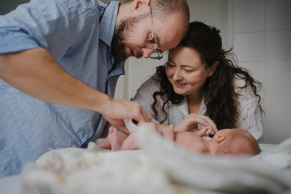 Mama und Papa sind mit Neugeborenem im Bad und wechseln Windeln. Echte Familienfotografie in Graz aus dem Wochenbett.