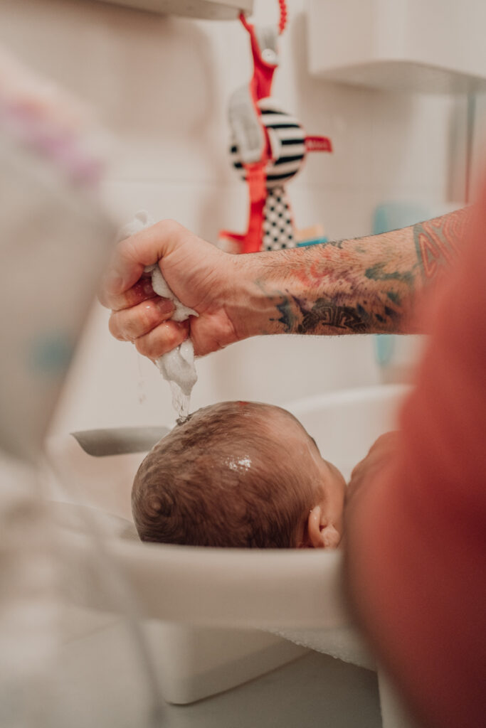 Papa wäscht seinem Baby mit einem Waschlappen die Haare – echter Badezeitmoment, dokumentarische Familienfotografie in Graz und Umgebung