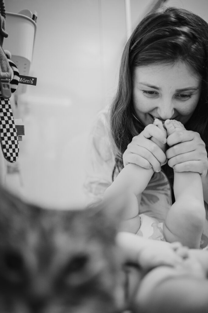 Mama küsst die Füße ihres Babys, während eine Katze im Vordergrund sitzt – liebevoller Familienalltag, dokumentarische Familienfotografie in Graz und Umgebung