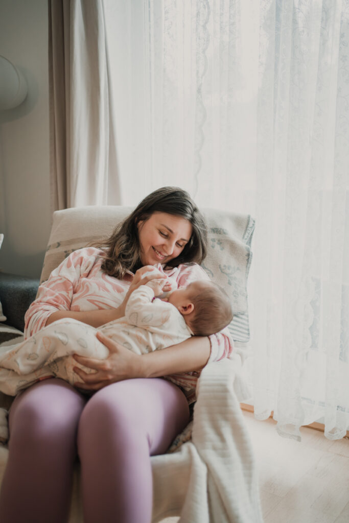 Mama gibt ihrem Baby das Fläschchen, während es ihren Finger hält – inniger Alltagsmoment, dokumentarische Familienfotografie in Graz und Umgebung