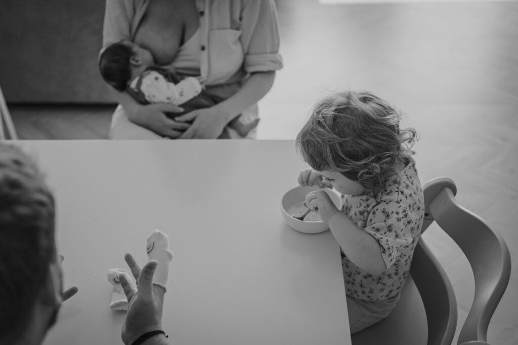 Stillende Mama mit Neugeborenem, Kleinkind isst Frühstück – authentischer Familienalltag im Wochenbett in Graz und Umgebung
