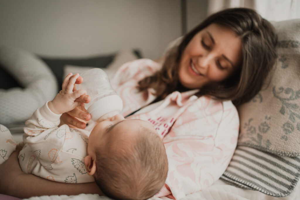 Mama gibt ihrem Baby das Fläschchen, während es ihren Finger hält – inniger Alltagsmoment, dokumentarische Familienfotografie in Graz und Umgebung