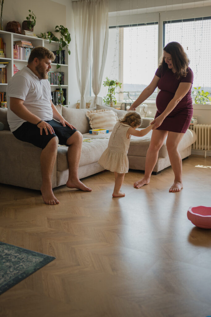 Schwangere Mama tanzt mit Kleinkind durch die Wohnung. Natürliche Schwangerschaftsfotografie in Graz.