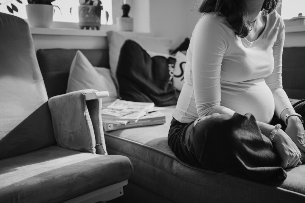 Schwangere Mama sitzt auf dem Sofa. So kann natürliche babybauchfotografie aussehen. aufgenommen von einer Familienfotografin in Graz.