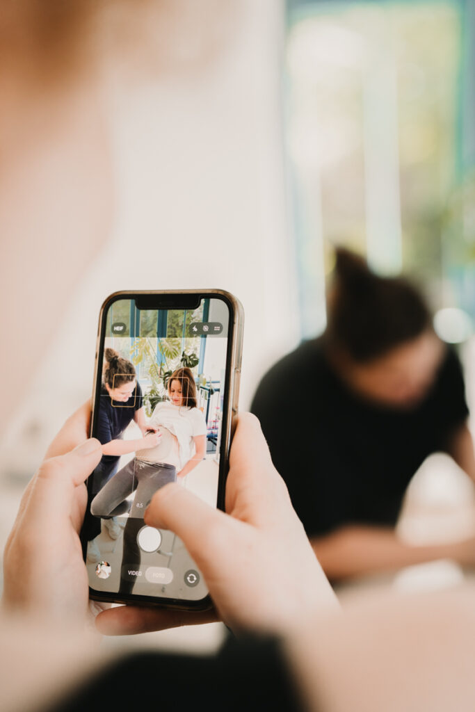 Während einer Baby Belly Bowl Session fotografiert eine Freundin die Schwangere Mama beim Anpassen der Baby Bowl. Festgehalten von einer Fotografin aus Graz, die dokumentarische Business Fotografie anbietet.