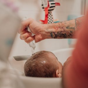Papa wäscht seinem Baby mit einem Waschlappen die Haare – echter Badezeitmoment, dokumentarische Familienfotografie in Graz und Umgebung
